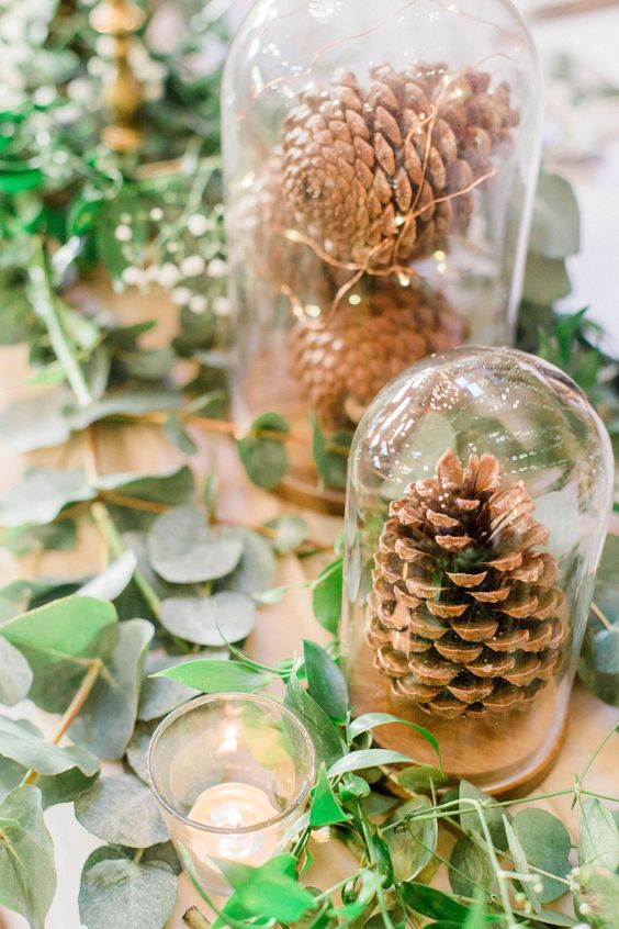 an all-natural wedding centerpiece of cloches with pinecones and lights, greenery on the table and some candles
