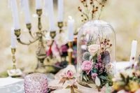 an enchanted forest wedding centerpiece of moss, a wood slice, a cloche with blooms and foliage and candles around