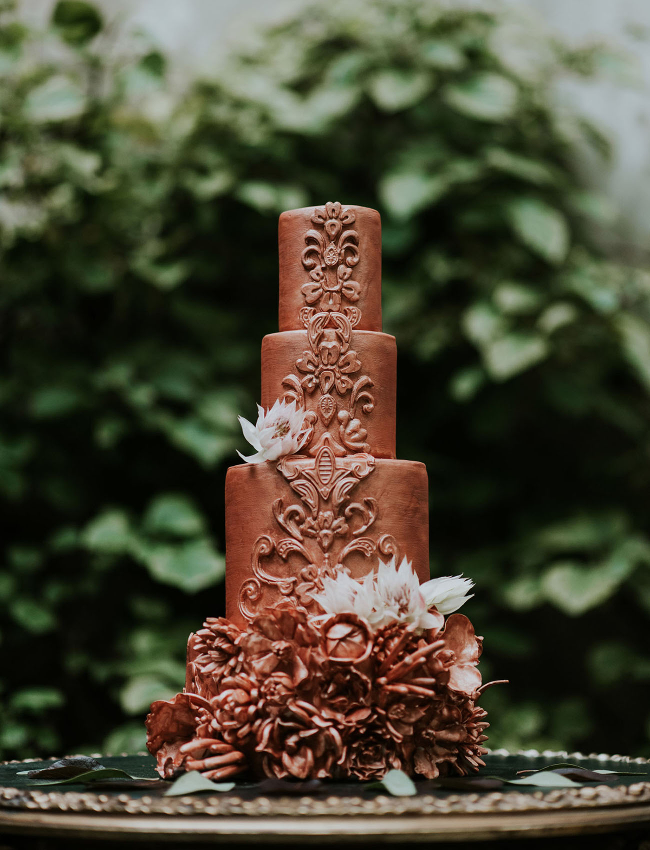 A copper wedidng cake with textural decor and edible flowers