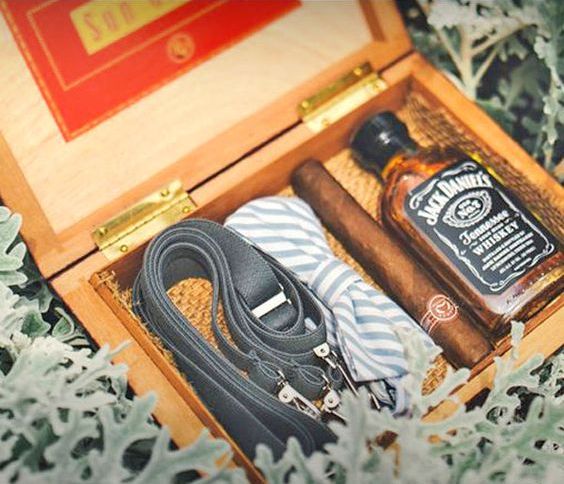 a box with a bow tie, suspenders, whiskey and a cigar is eveyrthing that a groomsman needs