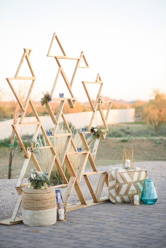 light-colored wooden triangle wedidng backdrop with greenery and candles for a desert ceremony