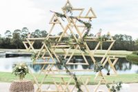 21 light-colored wooden triangle wedding backdrop covered with greenery garlands