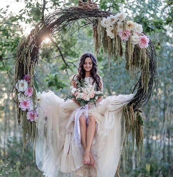a grapevine wreath with pink flowers used as a swing for the bride