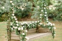29 a swinging bench decorated with leaves and white blooms for the couple