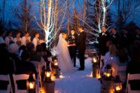 29 candle lanterns standing on tree stumps for warming up a winter wedidng aisle