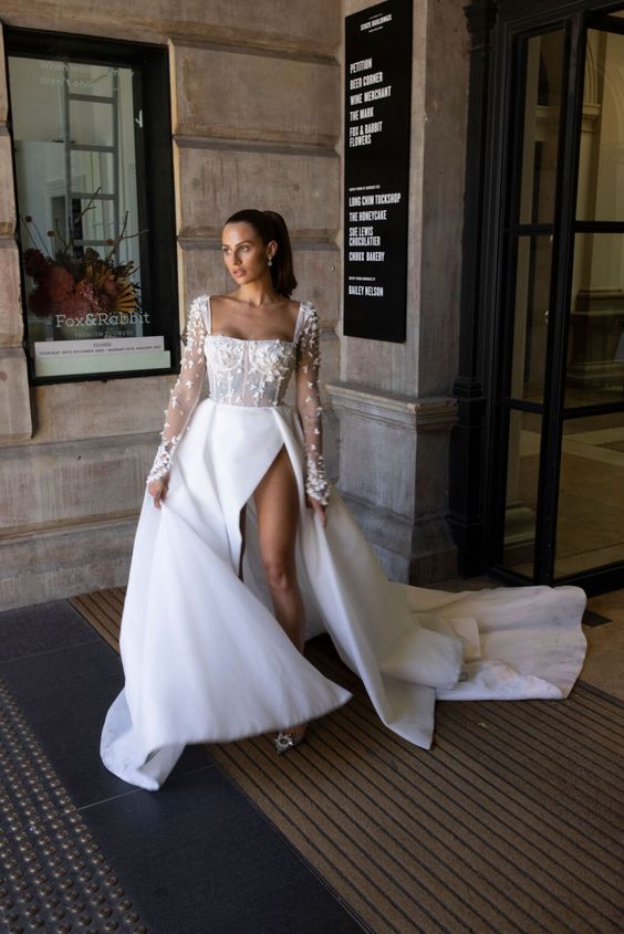 a creative modern wedding dress with a floral applique bodice with a square neckline and a plain skirt with a high slit and a train