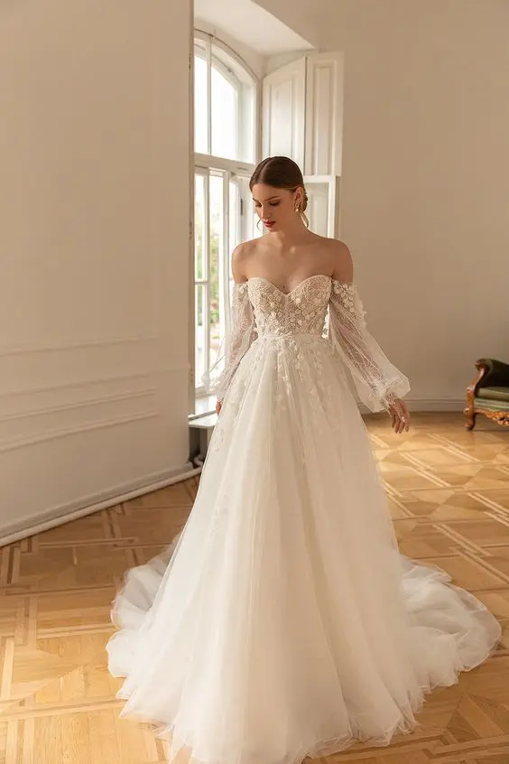 a dreamy off the shoulder wedding dress with a floral applique bodice and sleves and a layered skirt with a train