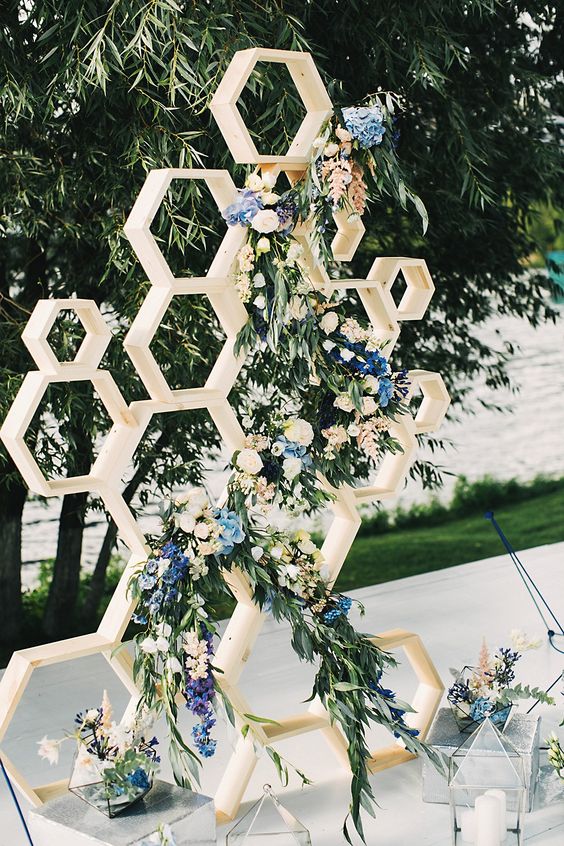 a honeycomb wedding backdrop decorated with lush greenery, neutral and blue flowers
