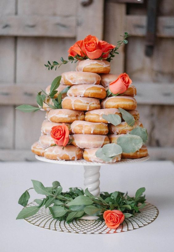 a stack of glazed donuts topped with foliage and fresh roses