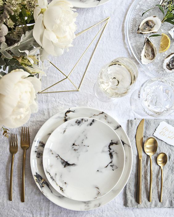 neutral wedding tablescape with gold flatware, neutral florals and marble plates and a charger