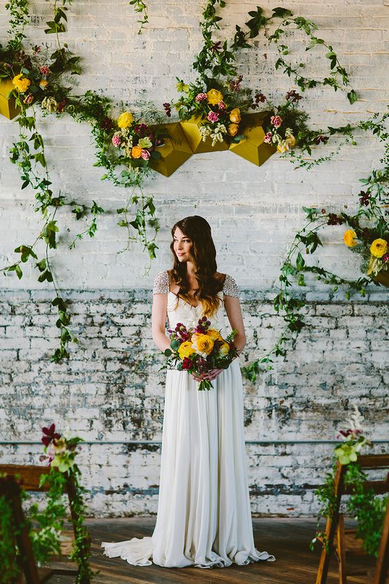 a mustard faceted geometric backdrop with matching florals and a bridal bouquet with the same blooms