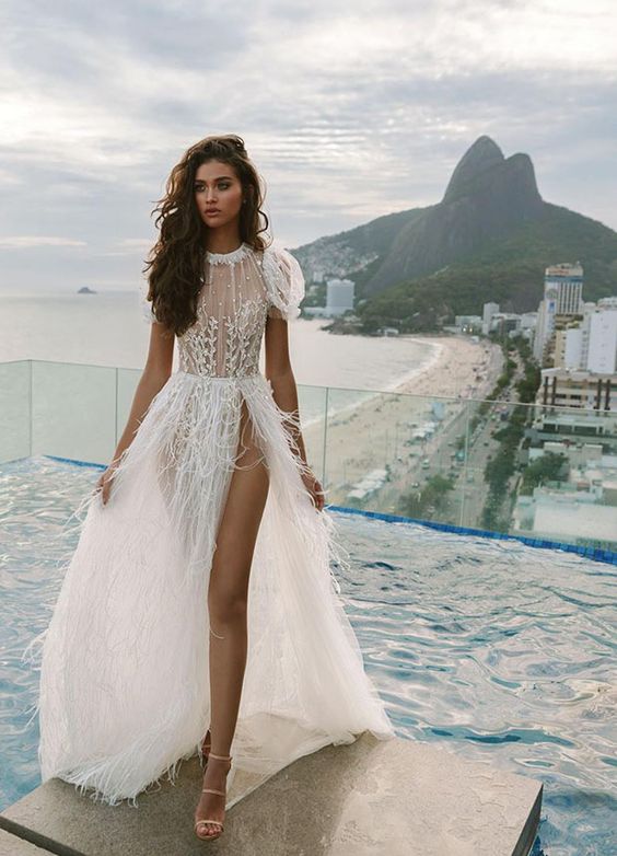 a glam bridal look with an embellished A-line wedding dress with strategically placed lace on the bodice, puff sleeves and a feather skirt with a thigh high slit