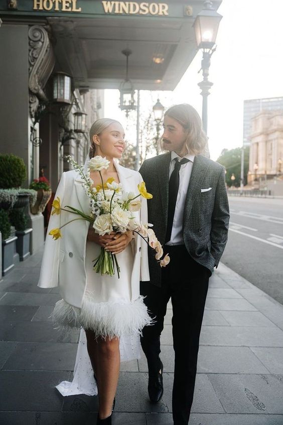 a modern bridal look with a plain feather over the knee wedding dress, a matching blazer and black shoes for a city hall wedding