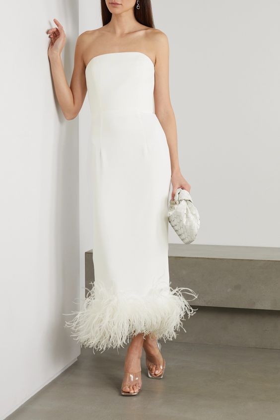 a plain fitting midi wedding dress with a feathered hem, clear shoes and a clutch are a gorgeous bridal look