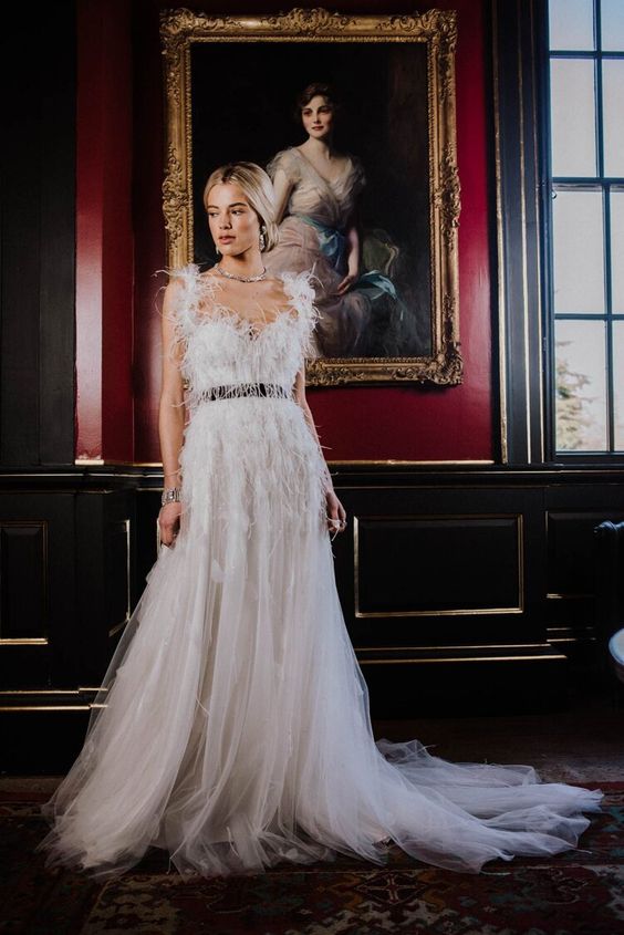 A sophisticated A line wedding dress with a feathered bodice and straps, a V neckline and a tulle skirt with a train is wow