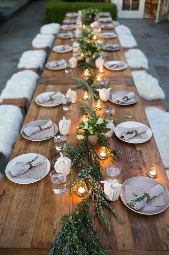 a cozy rustic tablescape with a greenery runner, candles and napkins accessorized with greenery and leather