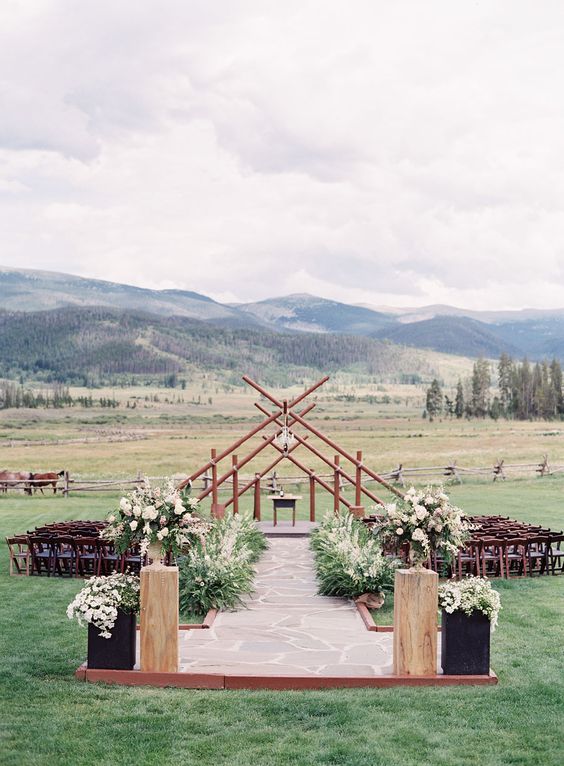 a gorgeous space with a stone aisle, lush greenery and wheat, wooden arches with a gorgeous view