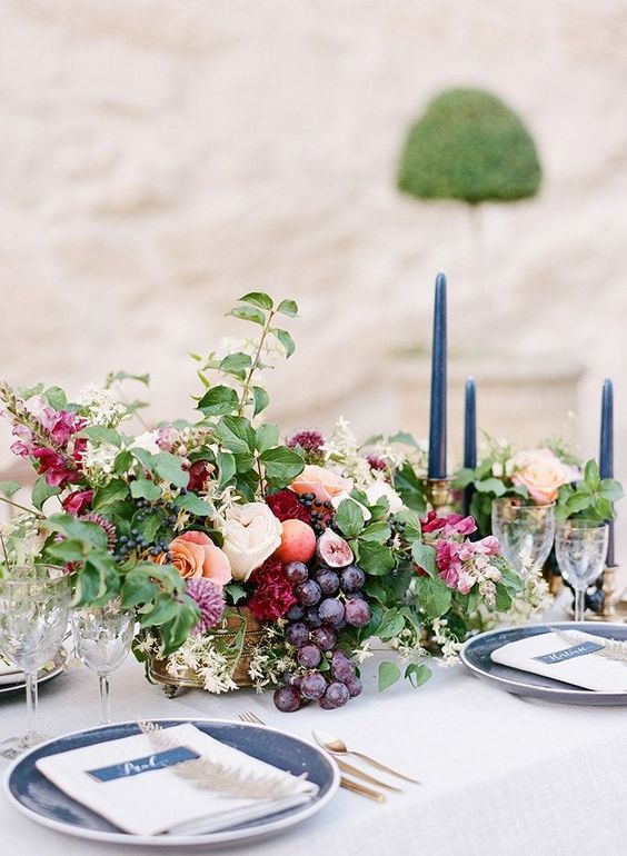 a beautiful centerpiece with blush and burgundy blooms, leaves and grapes in a gold bowl