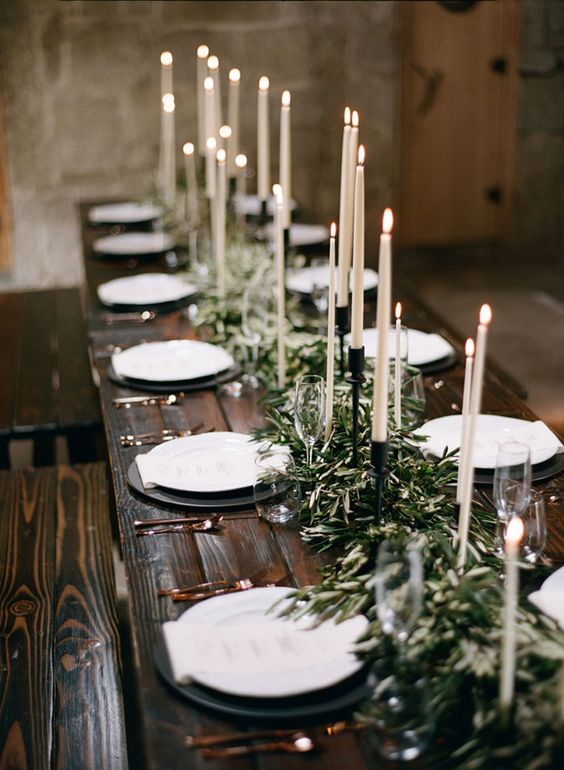 une table en bois teinté foncé avec un chemin de table en rameaux d'olivier et des bougies