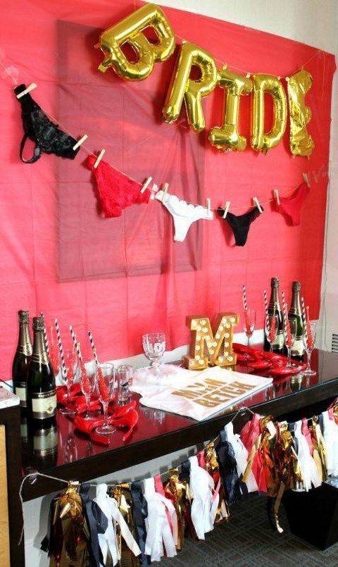 a fun drink station with a red wall, gold balloons and a panties garland