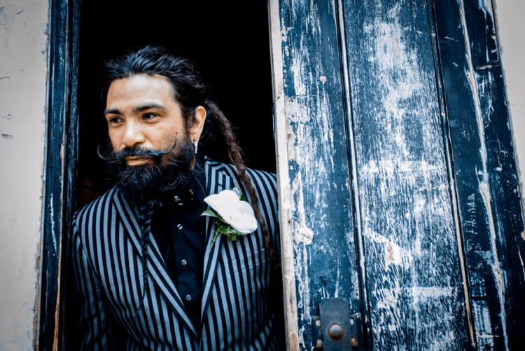 The groom was wearing a striped suit, a black shirt, a crazy hairstyle and a braided beard with a moustache