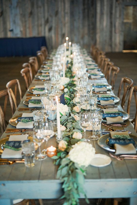 a tablescape with a lush greenery and peachy bloom runner, candles and copper flatware