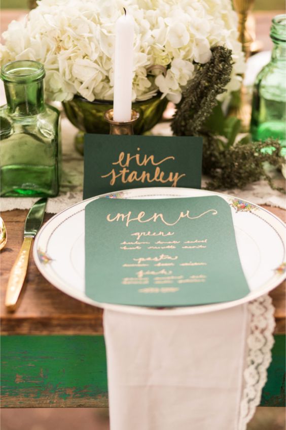 a wedding tablescape with an emerald menu and place card, emerlad glass vases