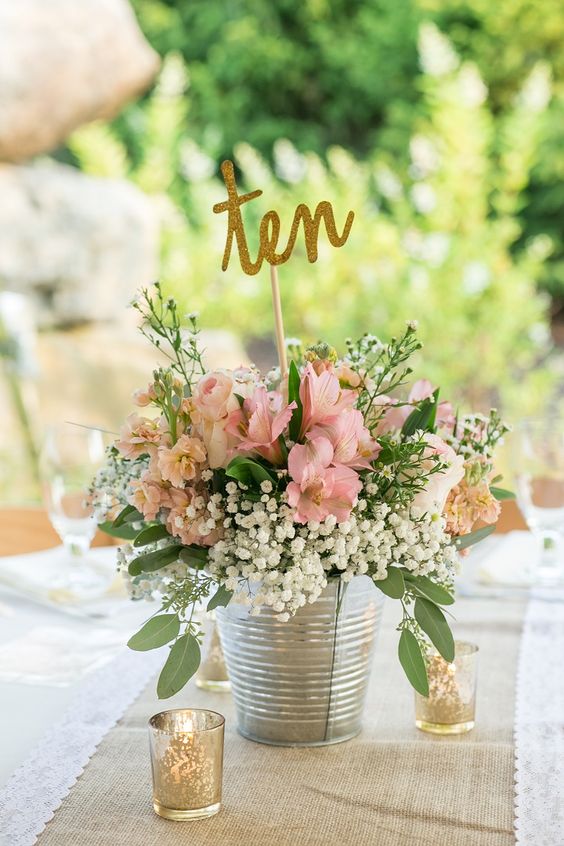 a bucket with a pink floral arrangement and a glitter table number