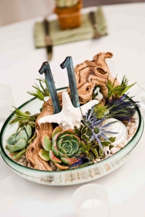 a glass bowl with driftwood, succulents, starfish and table numbers will be amazing on a beach wedding table