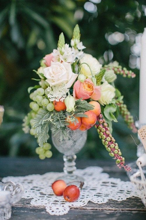 a crystal vase with white and peachy roses, green grapes and fruits for a relaxed summer wedding