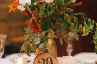 16 a wood slice with a wooden table number, a candle holder, a small pumpkin and a bold floral arrnagement will be a cool centerpiece