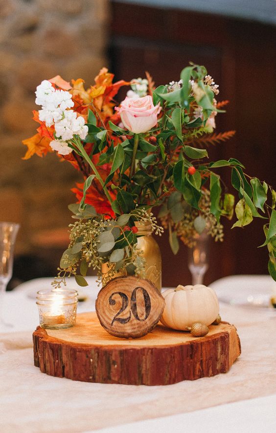 a wood slice with a wooden table number, a candle holder, a small pumpkin and a bold floral arrnagement will be a cool centerpiece