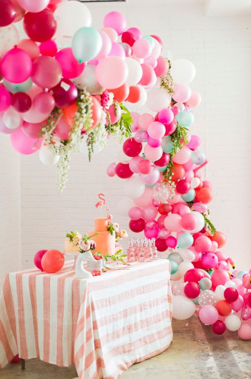 colorful balloon and tropical leaf arch over a dessert table