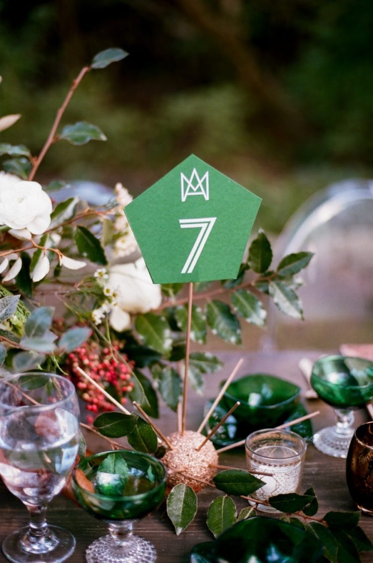 glitter copper ball with sticks and an emerald table number, greenery and emerald glasses