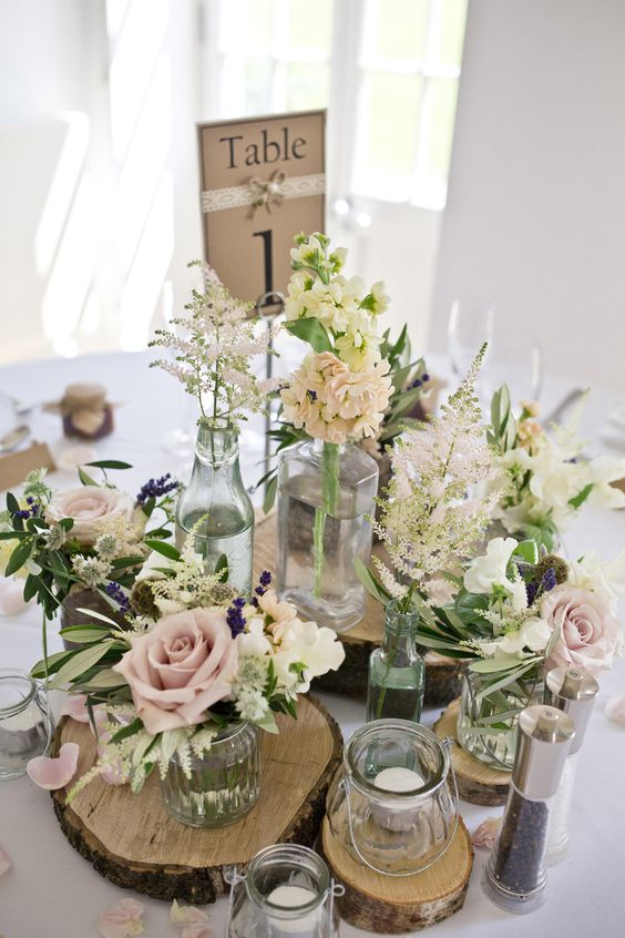 a rustic centerpiece with wood slices, various flower arrangements, candles and a table number