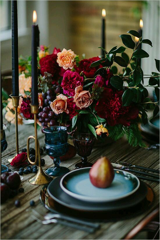 a colorful centerpiece with red, orange flowers, ferns and grapes for a moody fall wedding