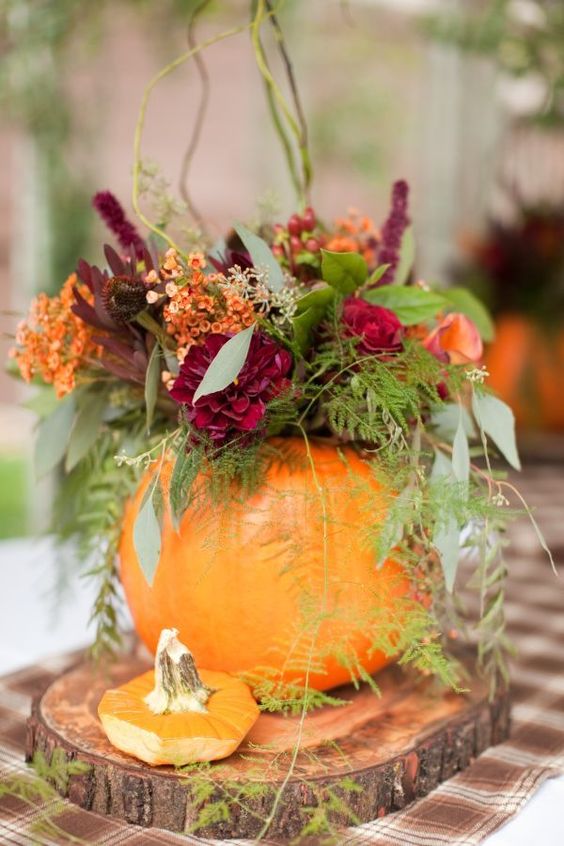a pumpkin vase with a colorful floral and greenery arrangement as a fall wedding centerpiece