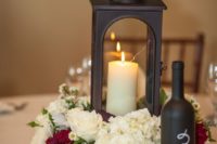 21 a dark metal lantern with a candle inside and a white and red bloom arrangement, a chalkboard bottle table number for a vineyard wedding