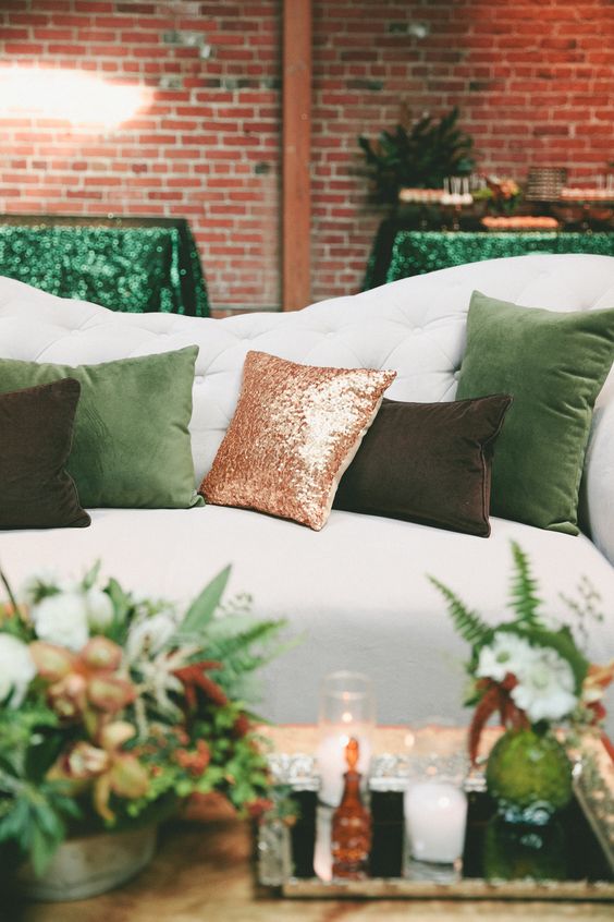 a cozy wedding lounge with emerald and copper glitter pillows, a green glass vase and ferns