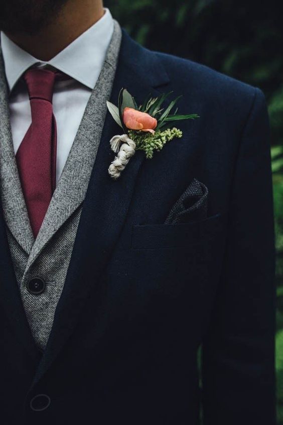 a navy suit, a grey waistcoat, a neutral shirt and a maroon tie