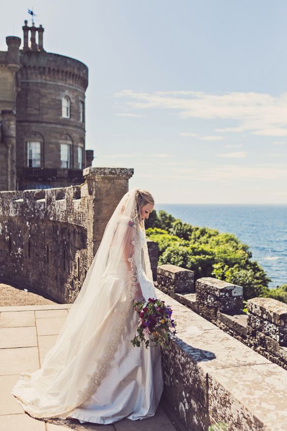 gorgeous bride in a refined dress and a veil standing on a castle wall