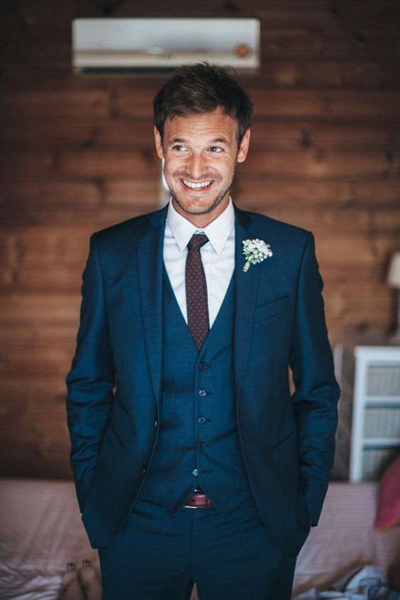 a navy three piece wedding suit with a burgundy tie and a baby's breath boutonniere