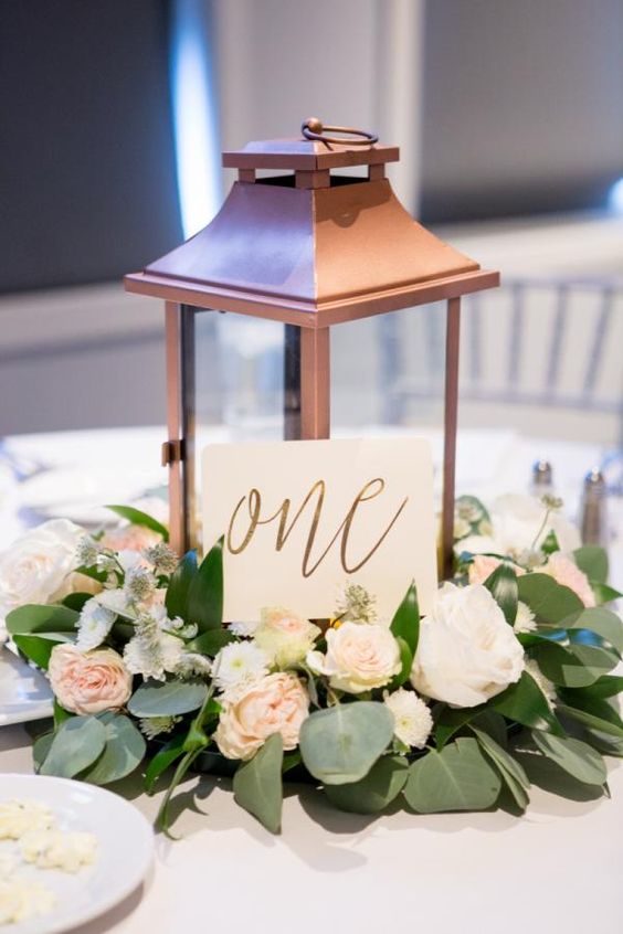 a copper lantern with a calligraphy table number and pastel flowers and leaves