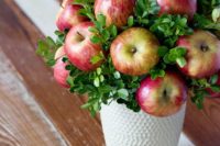 25 a white textural vase and an arrangement of boxwood and apples is an inexpensive and cute fall centerpiece