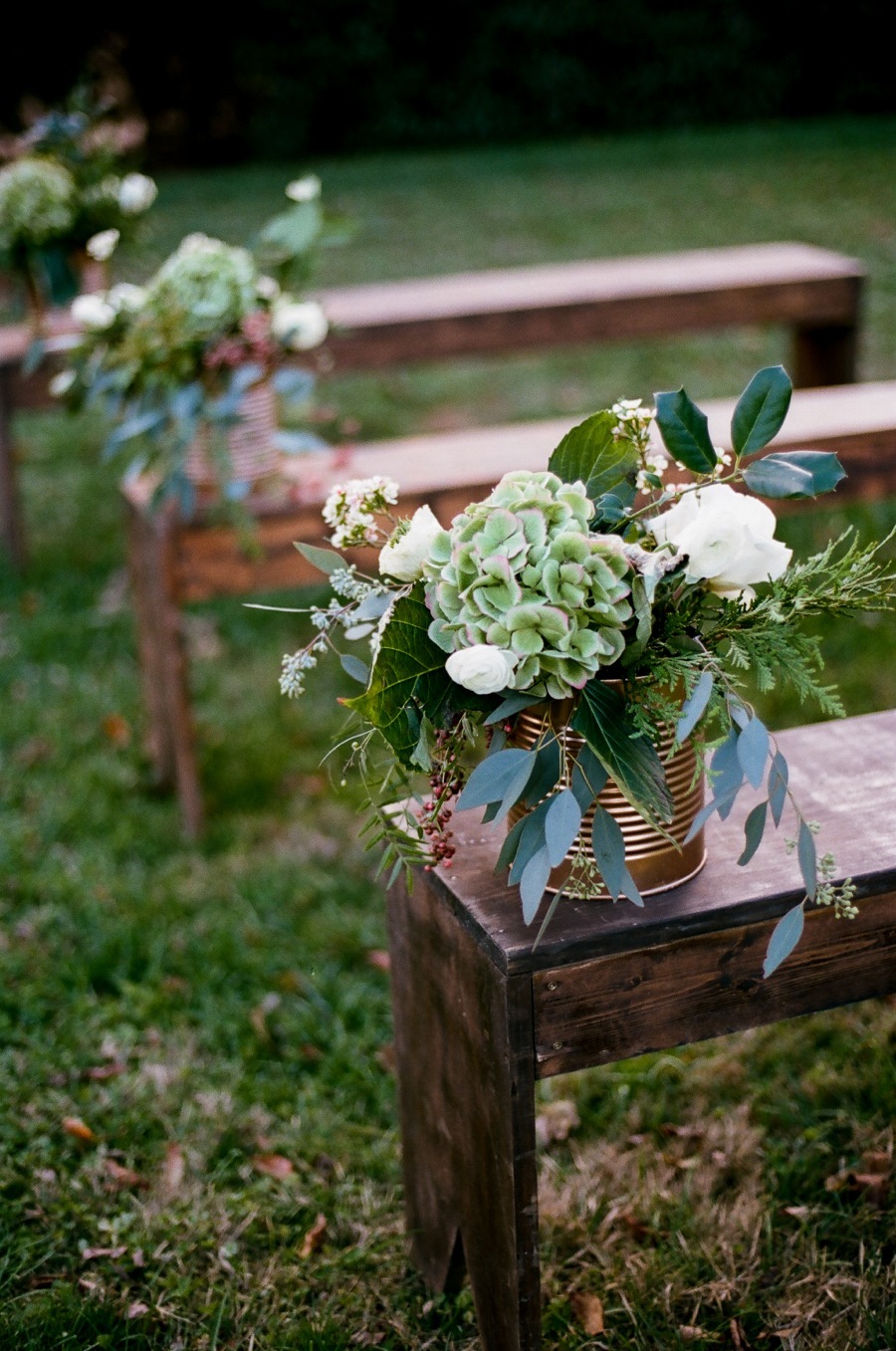 Copper tin cans with greenery and white blooms for lining up the aisle