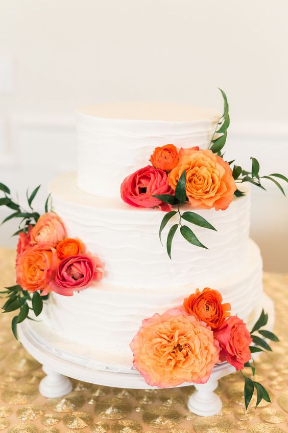 A white cake topped with orange and pink flowers is a chic idea