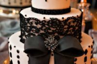 27 a white wedding cake decorated with beads and black lace, with a large edible bow for an elegant wedding