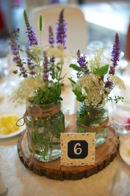 a wood slice, a chalkboard table number, jars wrapped with twine and wildflowers make up a cool centerpiece