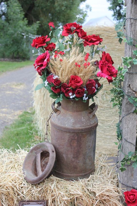 an old milk churn with red roses, greenery and wheat is awesome for any rustic celebration