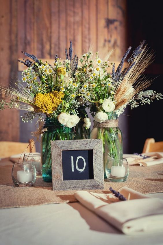 pots avec des fleurs sauvages, des bougies et un numéro de table encadré pour un joli paysage de table rustique